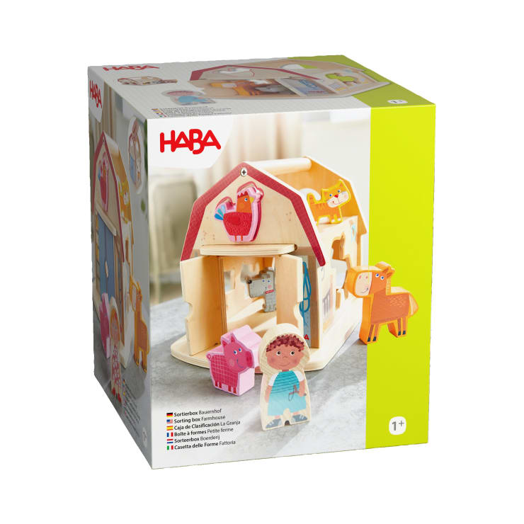 Eine Schachtel mit einem Holzspielzeug-Set der Marke HABA für Kinder ab 1 Jahr mit einer Scheune, Tierfiguren und einer Kinderfigur auf einem weißen Hintergrund.