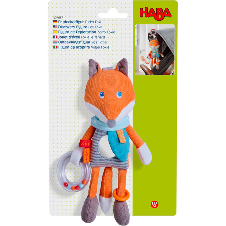 Ein Plüschfuchs mit blauem Halstuch, Ringrassel und Beißring ist an einem Kinderwagen befestigt. Die Verpackung zeigt die Marke HABA und den Produktnamen Discovery Figure Fox Foxy in mehreren Sprachen.