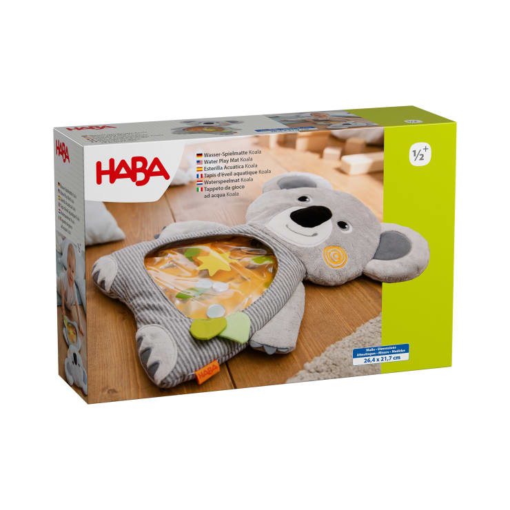 Ein verpacktes Produkt von HABA zeigt eine Wasserspielmatte in Form eines Koalas für Kleinkinder mit einem durchsichtigen Bauch, der mit schwimmenden Formen gefüllt ist. Die Verpackung enthält Produktdetails in mehreren Sprachen und ein Bild eines spielenden Babys im Hintergrund.