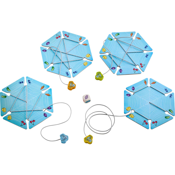 Vier sechseckige blaue Spielbretter mit Spinnennetzmustern liegen auf einer weißen Fläche, jedes mit farbigen Spielsteinen und einer Schnur, an der eine Spinnenfigur befestigt ist. In der Mitte befindet sich ein sechsseitiger Würfel mit Symbolen.