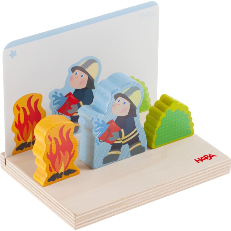 Ein Holzspielzeugset mit zwei Feuerwehrfiguren, zwei Flammen und einem grünen Busch auf einem Holzsockel. Auf der Rückseite befindet sich eine durchsichtige, aufrechte Platte mit einem Stern in der Ecke, und auf dem Sockel ist HABA aufgedruckt.