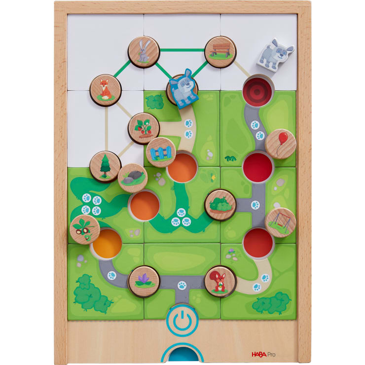 Ein Brettspiel aus Holz mit kreisförmigen Spielsteinen, die Tiere, Bäume und Häuser zeigen, die durch Linien verbunden sind. Der Hintergrund besteht aus grünen Feldern, Wegen und farbigen Kreisen. Ein blaues Machtsymbol befindet sich in der unteren Mitte.
