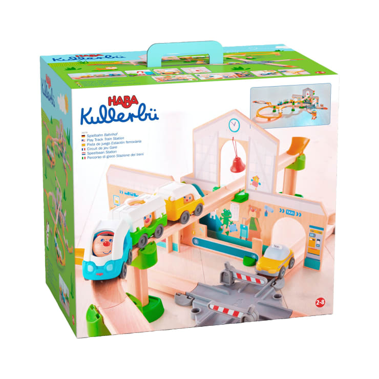 Abgebildet ist ein Karton für das HABA Kullerbü-Spielzeugeisenbahn-Set. Auf der Verpackung sind Bilder des zusammengebauten Holzeisenbahn-Sets mit Gleisen, Fahrzeugen und einem Bahnhof abgebildet. Die Schachtel hat einen grünen Griff und ein buntes Design.
