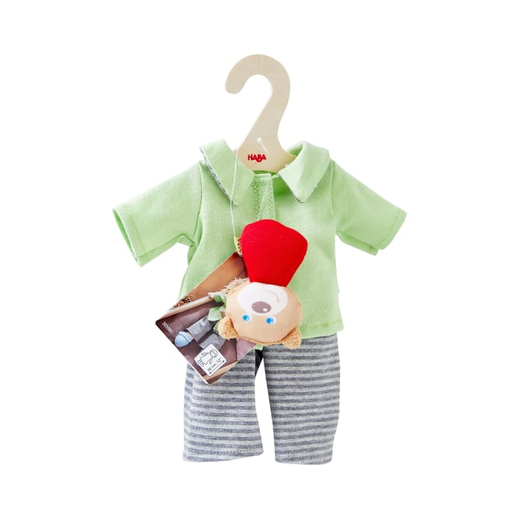 Ein Puppenoutfit auf einem Bügel umfasst ein hellgrünes Hemd, eine grau-weiß gestreifte Hose und eine Umhängetasche mit einem kleinen Plüschtier.