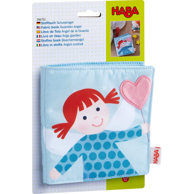 Ein Stoffbuch für Kinder namens Schutzengel von HABA wird in seiner Verpackung gezeigt. Das Buch zeigt eine Illustration eines Engels mit rotem Haar, der ein rosa Herz auf dem Cover hält.