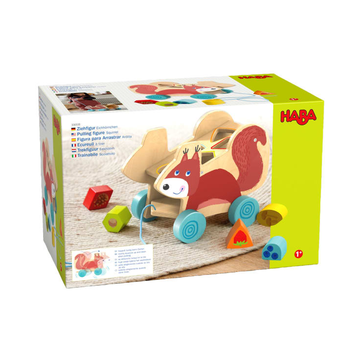 Schachtel mit einem HABA-Nachziehspielzeug aus Holz in Form eines Eichhörnchens, daneben sind bunte geometrische Blöcke abgebildet. Die Verpackung ist hauptsächlich gelb und enthält Produktbilder und Informationen in mehreren Sprachen.