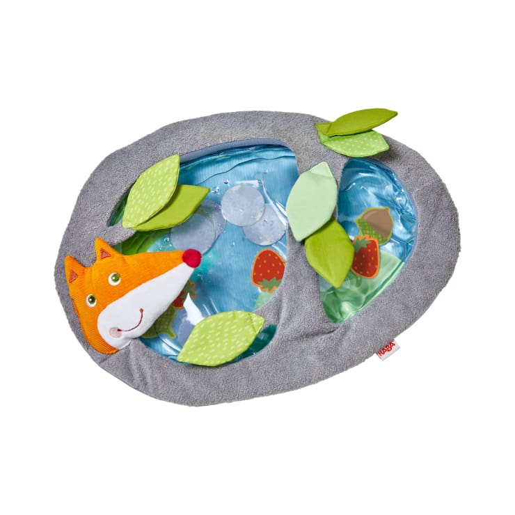 Ein weiches, ovales Babyspielzeug mit einem plüschigen, orangefarbenen Fuchsgesicht, grünen Stoffblättern und einem durchsichtigen Teil mit Wasser und schwimmender Erdbeergrafik im Inneren, alles umrandet von grauem Stoff.