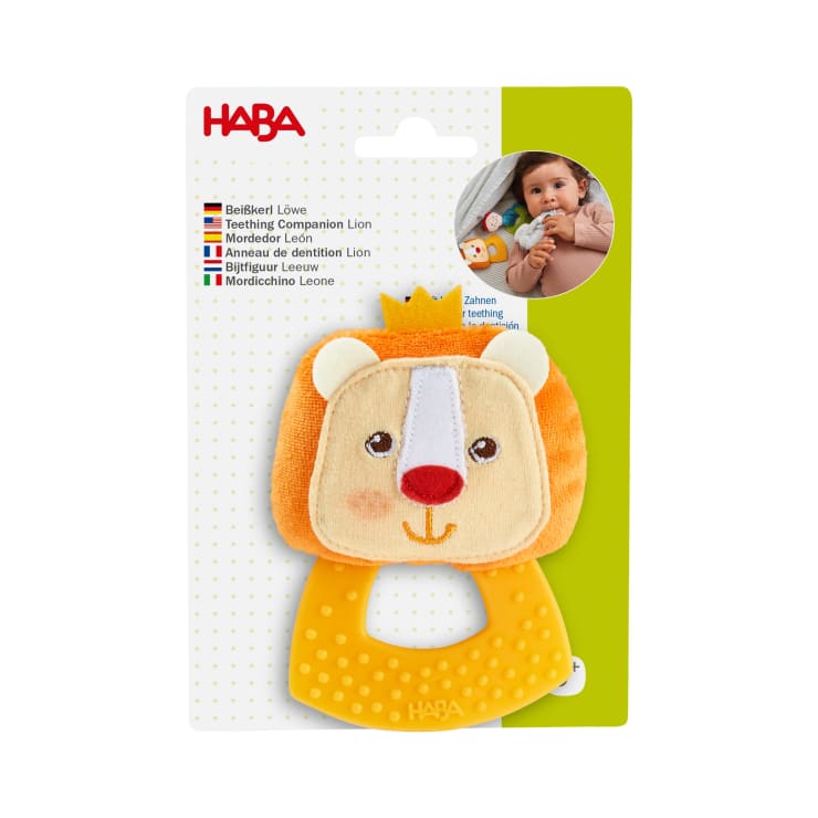 Die Verpackung zeigt ein HABA-Beißspielzeug in Form eines Löwen mit einem gelben, strukturierten Griff. Auf der Verpackung sind ein Foto eines Babys, das das Spielzeug hält, und Produktinformationen in mehreren Sprachen abgebildet.