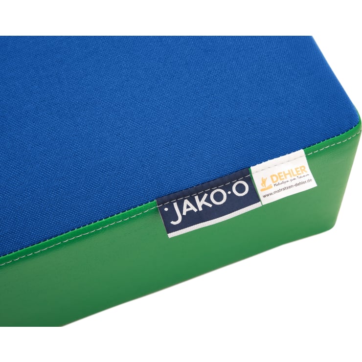 Nahaufnahme eines rechteckigen Kissens oder einer Matte mit einer blauen Stoffoberfläche, grünen Seiten und Etiketten mit der Aufschrift JAKO-O und DEHLER an der Naht.
