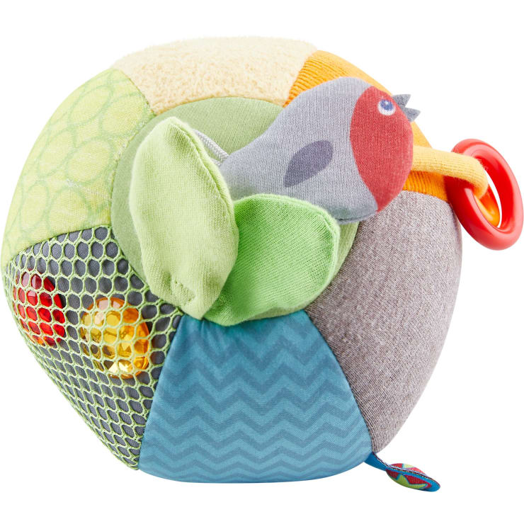 Ein mehrfarbiger Plüschball mit verschiedenen Stoffstrukturen, mit einem ausgestopften Vogel an der Spitze, grünen Stoffflügeln, einem roten Kunststoffring und einem Netzabschnitt, der kleine Kunststoffkugeln enthält.