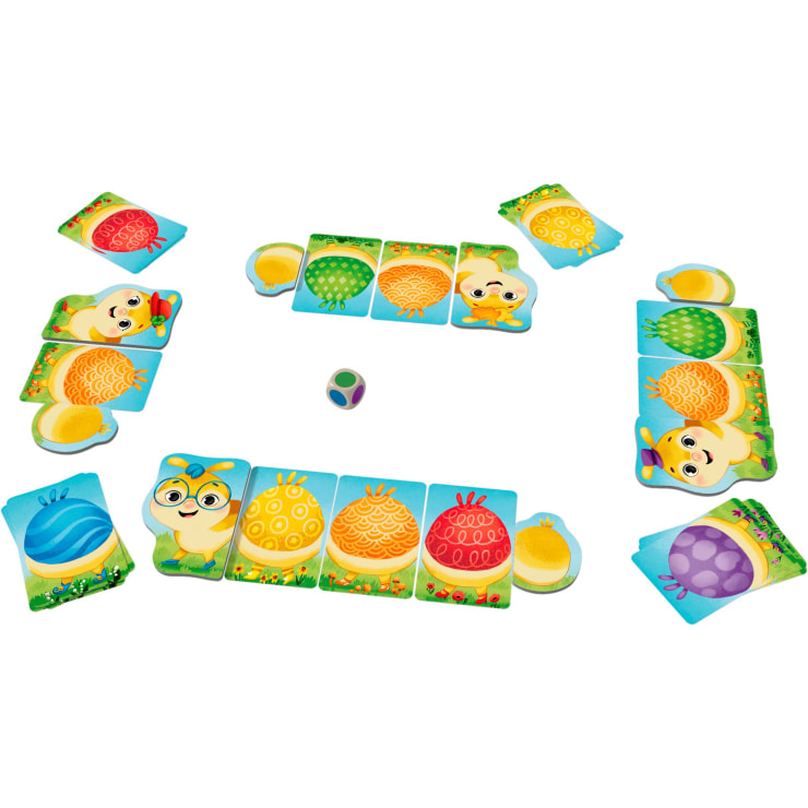Ein Brettspiel für Kinder wird aufgebaut. Vier Charakterkarten, jede mit einer Raupe und farbigen Segmenten, liegen an vier Ecken. Ein mehrfarbiger Würfel liegt in der Mitte. Farbige Karten sind auf dem Spielfeld verteilt.