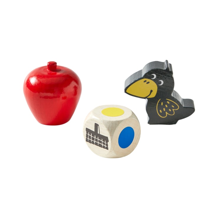 Ein roter Holzapfel, ein heller Holzwürfel mit farbigen Kreisen und einem Zaunsymbol sowie eine schwarze Holzvogelfigur mit gelbem Schnabel sind auf einem weißen Hintergrund angeordnet.