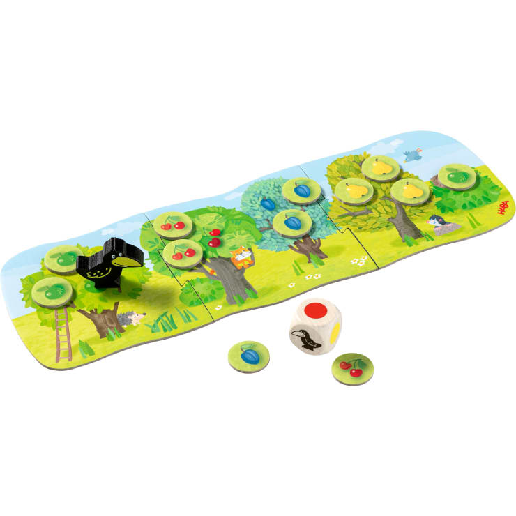 Das farbenfrohe Brettspiel besteht aus vier zusammenhängenden Feldern mit illustrierten Bäumen, runden Plättchen mit Früchten, einem schwarzen Holzvogel und einem Würfel mit Obst- und Vogelsymbolen, die auf einer Graslandschaft liegen.