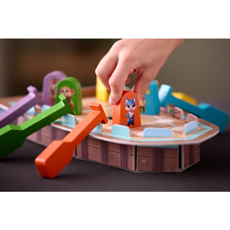 Eine Hand bewegt eine hölzerne Spielfigur mit einem Cartoon-Tier darauf über ein Spielbrett aus Pappe, das wie ein Schiff geformt ist, mit bunten Hebeln und anderen Tierfiguren.