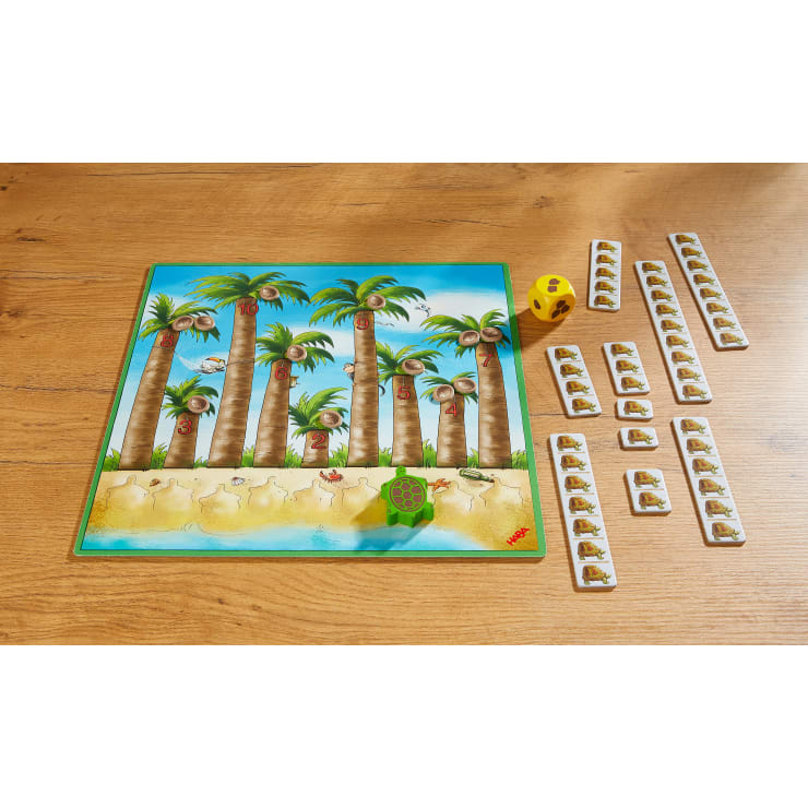 Ein Brettspiel mit einem tropischen Palmenmotiv, das ein Spielbrett mit nummerierten Bäumen, eine grüne Schildkröte, einen gelben sechsseitigen Würfel und mehrere Reihen von rechteckigen Spielsteinen mit Illustrationen zeigt, die auf einem Holztisch liegen.