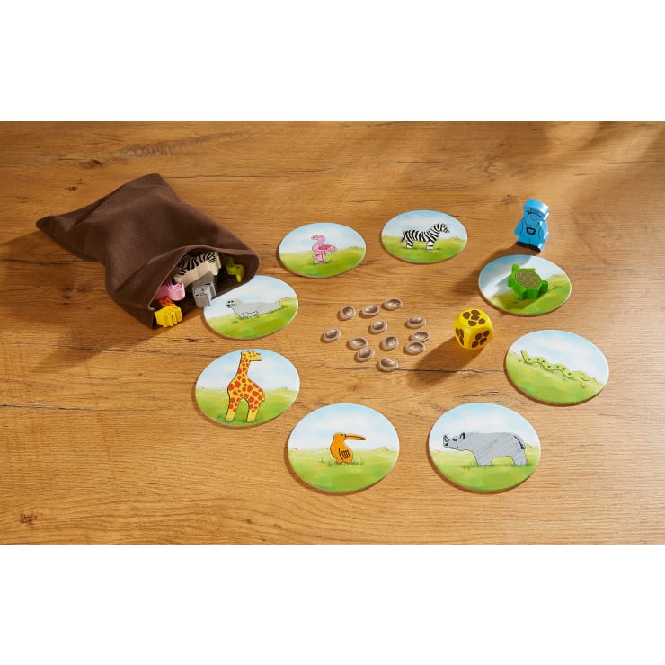 Aus einem braunen Stoffbeutel werden Tierplättchen auf eine Holzfläche geschüttet. Kreisförmige Tierkarten, ein gelber Würfel und kleine ovale Spielsteine sind in einem losen Kreis um den Beutel herum angeordnet.