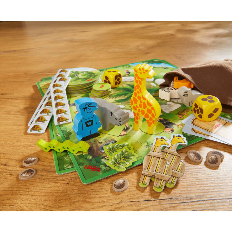 Auf einem Holztisch wird ein Kinderbrettspiel mit Tierfiguren aus Holz, Spielsteinen, Würfeln, Karten und illustrierten Spielbrettern mit Zoo- oder Safarithematik aufgebaut.
