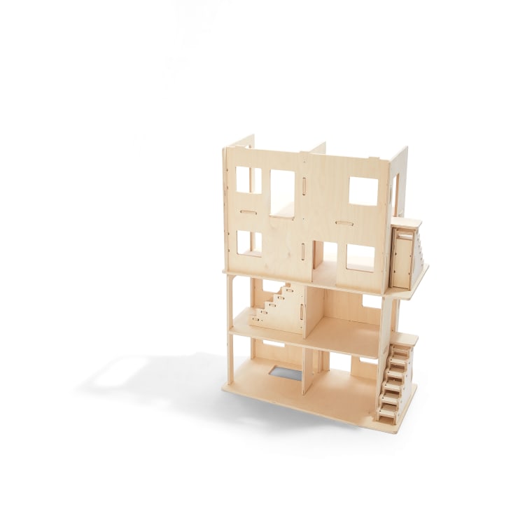 Ein schlichtes, unfertiges Puppenhaus aus Holz mit zwei Stockwerken, sichtbarer Treppe und mehreren Fenster- und Türöffnungen vor einem weißen Hintergrund.