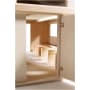 Nahaufnahme eines kleinformatigen Architekturmodells aus Holz, das einen Raum mit vier hölzernen bankähnlichen Strukturen und einem Fenster an der rechten Wand zeigt. Die Tür auf der rechten Seite ist teilweise geöffnet.