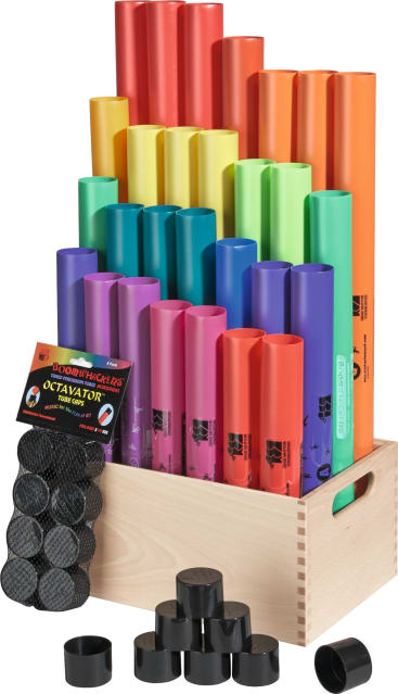 Eine Holzkiste enthält bunte Boomwhackers-Röhren aus Plastik, die nach Größe und Farbe geordnet sind. Schwarze Plastikkappen, Octavators genannt, sind vor der Kiste verstreut und ein beschriftetes Octavator-Set ist darin verstaut.