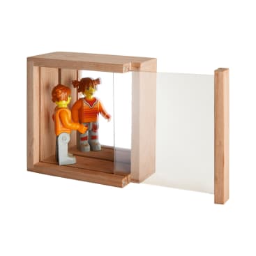 Eine Holzkiste mit einer durchsichtigen Scheibe auf einer Seite enthält eine Spielzeugfigur, die ihr Spiegelbild in der Kiste betrachtet. Die Kiste hat eine offene Seite, die die spiegelnde Oberfläche zeigt.