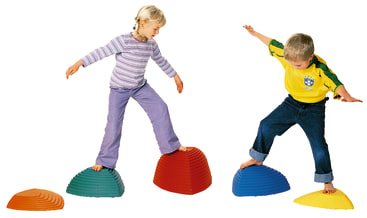 Zwei kleine Kinder balancieren auf bunten Plastik-Trittsteinen. Das Mädchen steht auf einem roten Stein, der Junge auf einem blauen. Sie strecken ihre Arme aus, um das Gleichgewicht zu halten, und scheinen miteinander zu spielen.