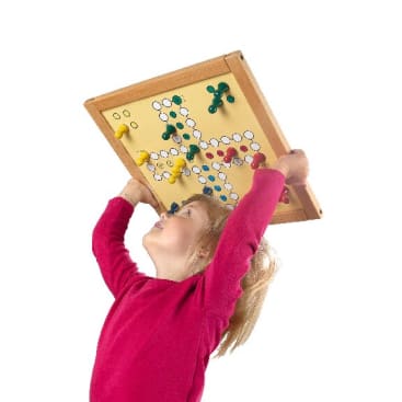 Ein kleines Kind in einem roten Hemd hält ein Ludo-Spielbrett über seinen Kopf und schaut es an. Das Brett hat farbige Spielsteine und einen weißen Hintergrund. Der Bildhintergrund ist einfarbig weiß.