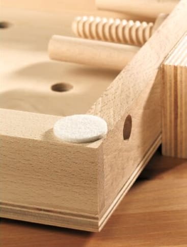 Nahaufnahme eines Holzspiels oder -puzzles mit glattem, hellem Holz, kreisrunden Löchern, Dübeln und einer weißen Filzunterlage in der Ecke.
