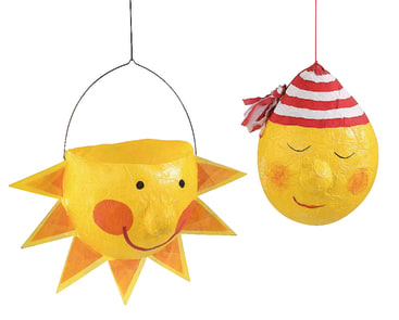 Zwei gelbe Papierlaternen, eine in Form einer lächelnden Sonne mit orangefarbenen Strahlen und einem Henkel, die andere in Form eines runden Gesichts mit geschlossenen Augen, rosigen Wangen und einem rot-weiß gestreiften Hut, hängen vor einem weißen Hintergrund.