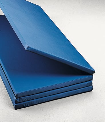 Ein Stapel blauer, faltbarer Gymnastikmatten, wobei eine Matte teilweise aufgeklappt ist und auf den anderen liegt, auf einer hellen Fläche.