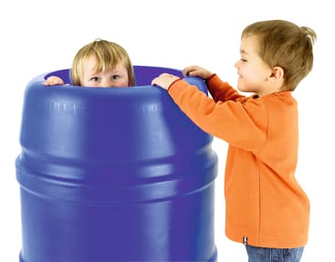 Zwei kleine Kinder spielen mit einem großen blauen Plastikfass. Ein Kind ist im Inneren des Fasses und schaut heraus, während das andere Kind, das ein orangefarbenes Hemd trägt, daneben steht und das Kind im Inneren betrachtet.