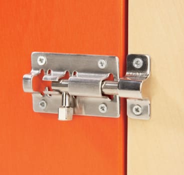 Nahaufnahme eines silbernen Metallschieberiegels, der an der Kante einer orangefarbenen und hellen Holztür oder eines Schranks befestigt ist. Der Riegel ist mit Schrauben befestigt.