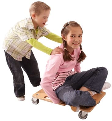 Ein Junge schiebt ein Mädchen, das auf einem hölzernen Rollbrett mit Rädern sitzt. Beide Kinder scheinen zu lächeln und zusammen vor einem schlichten weißen Hintergrund zu spielen.