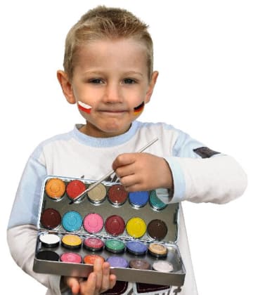 Ein kleiner Junge hält ein offenes Farbset und einen Pinsel in der Hand. Er hat die polnische und die deutsche Flagge auf seine Wangen gemalt. Er trägt ein helles, langärmeliges Hemd und schaut in die Kamera.