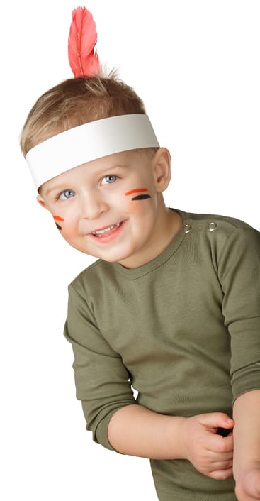 Kleines Kind mit hellem Haar, das ein grünes, langärmeliges Hemd, ein weißes Papierstirnband mit einer roten Feder und rote Gesichtsbemalung auf den Wangen trägt und in die Kamera lächelt, vor einem weißen Hintergrund.