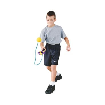 Ein Junge in einem grauen T-Shirt, schwarzen Shorts und schwarzen Turnschuhen spielt mit einem Ball- und Becherspielzeug und konzentriert sich darauf, den gelben Ball zu fangen, der an einer blauen Schnur befestigt ist. Der Hintergrund ist weiß.