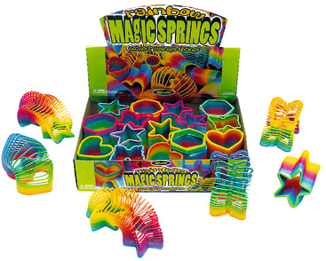 Eine Schachtel mit der Aufschrift Rainbow Magic Springs enthält bunte Plastikfedern in verschiedenen Formen, darunter Kreise, Sterne, Herzen und Schmetterlinge. Mehrere Federn sind um die Schachtel herum angeordnet.