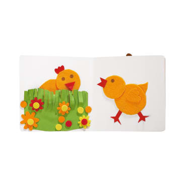 Ein Kinderbuch zeigt zwei gelbe Filzküken mit roten Schnäbeln und Füßen. Ein Küken steht inmitten von grünem Filzgras und Blumen; das andere Küken steht allein auf der gegenüberliegenden Seite, mit Blick nach links.