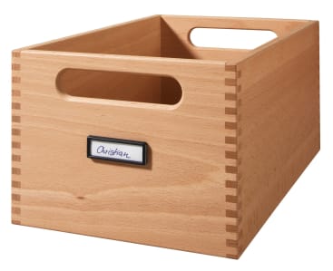 Eine Aufbewahrungsbox aus hellem Holz mit keilgezinkten Ecken, ausgeschnittenen Griffen an den Seiten und einem Etikettenhalter auf der Vorderseite, der einen handgeschriebenen Namen trägt.