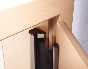 Nahaufnahme einer Holztür mit einer schwarzen, einziehbaren oder ziehharmonikaförmigen Barriere, die entlang der Kante zwischen Tür und Türrahmen angebracht ist.