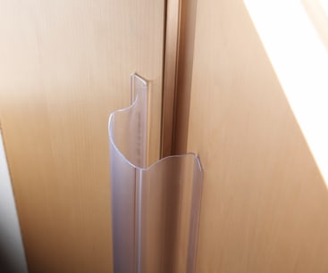 Ein Fingerschutz aus durchsichtigem Kunststoff wird an der Scharnierseite einer leichten Holztür angebracht, um zu verhindern, dass die Finger beim Schließen der Tür in den Spalt geraten.