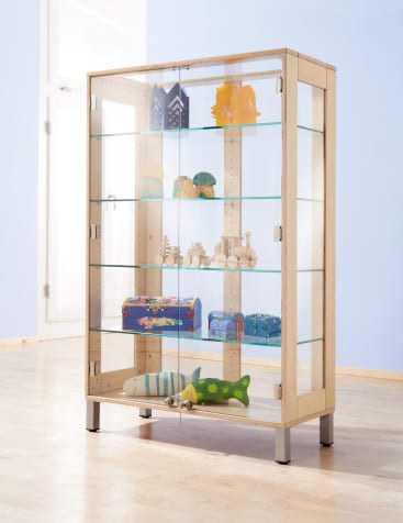 In einem hellen Raum mit hellem Holzboden und hellblauen Wänden steht eine Glasvitrine mit drei Einlegeböden, in denen verschiedene Holzspielzeuge, bunte Schachteln und kleine Dekorationsartikel aufbewahrt werden.