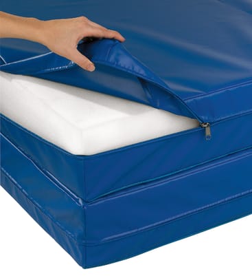 Eine Hand öffnet den blauen Bezug einer Schaumstoffmatratze und gibt den Blick auf das Innere aus weißem Schaumstoff frei. Die Matratze scheint für den medizinischen oder institutionellen Gebrauch hergestellt zu sein.