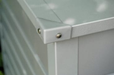 Nahaufnahme der Ecke eines weißen Metallkastens oder -schranks, die ein schützendes Metall-Eckstück zeigt, das mit zwei runden Schrauben befestigt ist.