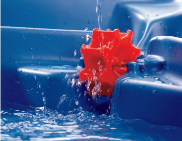 Ein Wasserstrahl fließt auf ein rotes Kunststoffrad in einem blauen Wasserspieltisch, wodurch sich das Rad dreht und das Wasser um es herum spritzt.