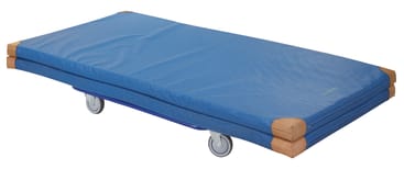 Eine blaue rechteckige Gymnastikmatte mit verstärkten braunen Ecken wird in der Hälfte gefaltet und auf einen Rollwagen mit vier grauen Rädern gelegt.