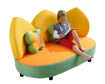 Ein junges Mädchen sitzt auf einem orange-grünen Sofa in Form von Blumenblättern und liest ein Buch. Auf dem Sofa befinden sich zwei dekorative Kissen, eines davon grün und in Form eines Schmetterlings. Der Hintergrund ist weiß.