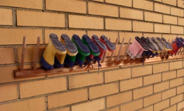 Eine Reihe kleiner Regenstiefel in verschiedenen Farben hängt kopfüber an Holzpflöcken, die an einer Ziegelwand befestigt sind.