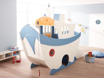 Ein Spielzimmer für Kinder mit einem großen, weiß-blauen Holzspielgerät in Form eines Bootes, mit maritimen Dekorationen, Spielzeug und Licht, das durch große Fenster einfällt.
