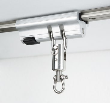 Nahaufnahme eines Metallschienensystems für die Decke mit einem Karabinerhaken und einem Schäkel, das zur Sicherung und Unterstützung von Lasten oder Geräten dient.